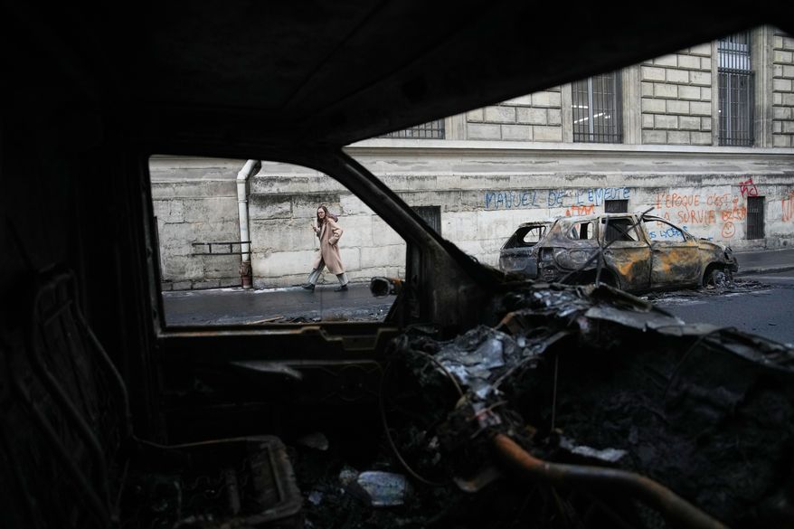 A woman walks past burned-out cars after a quiet night Monday under curfew, the first since weekend protests over the cost of living turned into rioting and looting across France, in Paris, Tuesday, Oct. 20, 2026. (AP Photo/Christophe Ena)
