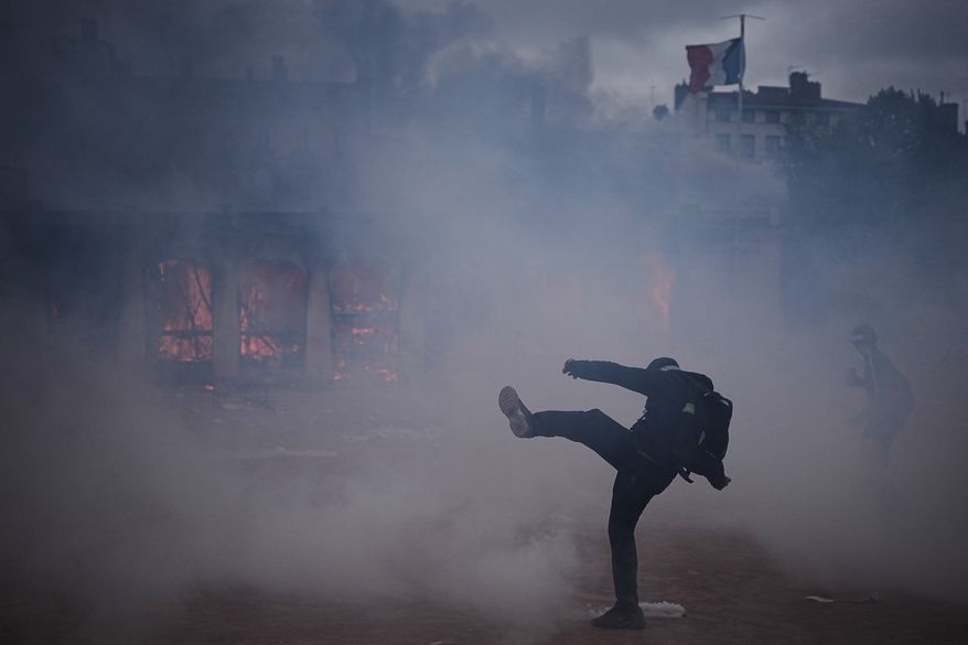 A protester kicks a tear gas canister in front of the burning tourism office during a demonstration against rising living costs and in solidarity with students’ grievances in Lyon, France, Saturday, Oct. 17, 2026. (AP Photo/Laurent Cipriani)