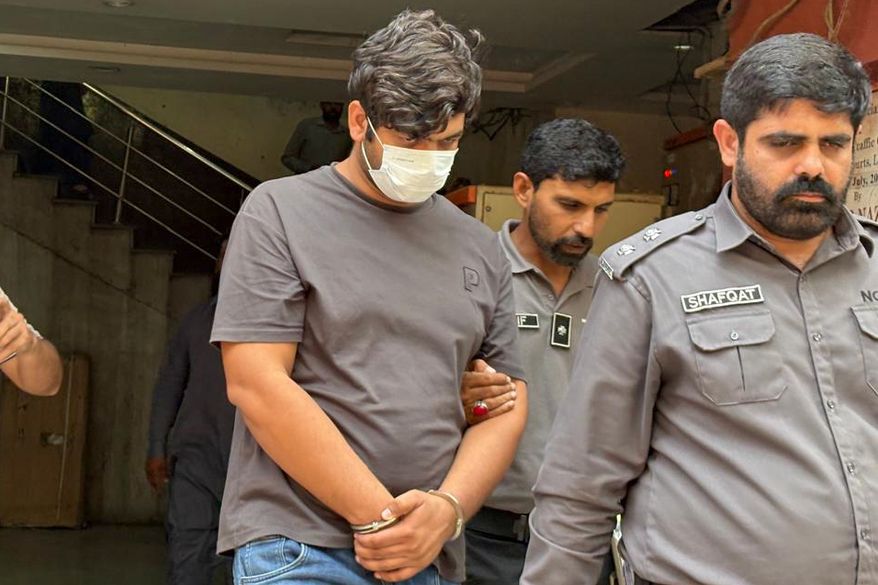 In this photo taken with a smartphone, police officers escort detained suspect Faheem Akram, accused of running an online counterfeit postage operation that U.S. prosecutors say caused more than $126 million in losses to the U.S. Postal Service, in Lahore, Pakistan, Wednesday, Oct. 21, 2026. (AP Photo/K.M. Chaudary)