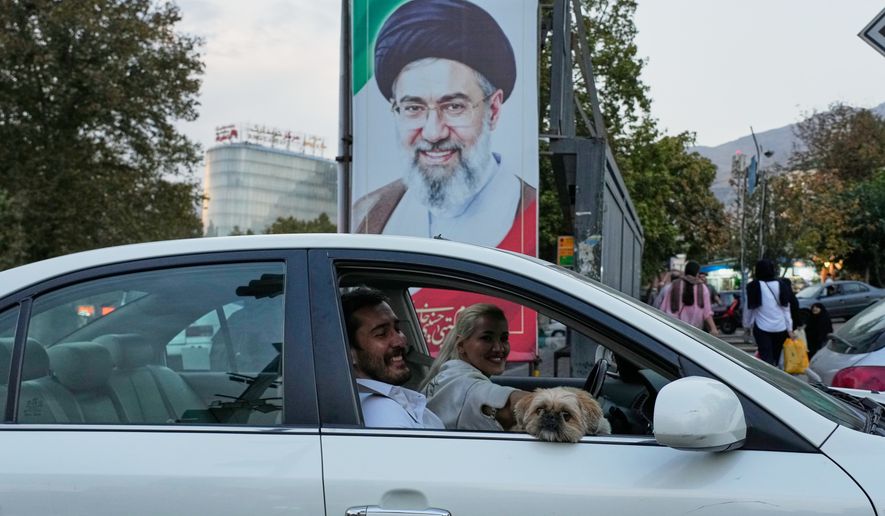 A man and a woman ride in a car with a dog past a portrait of Iran's Supreme Leader Mojtaba Khamenei in Tehran, Iran, Wednesday, Oct. 21, 2026. (AP Photo/Vahid Salemi)