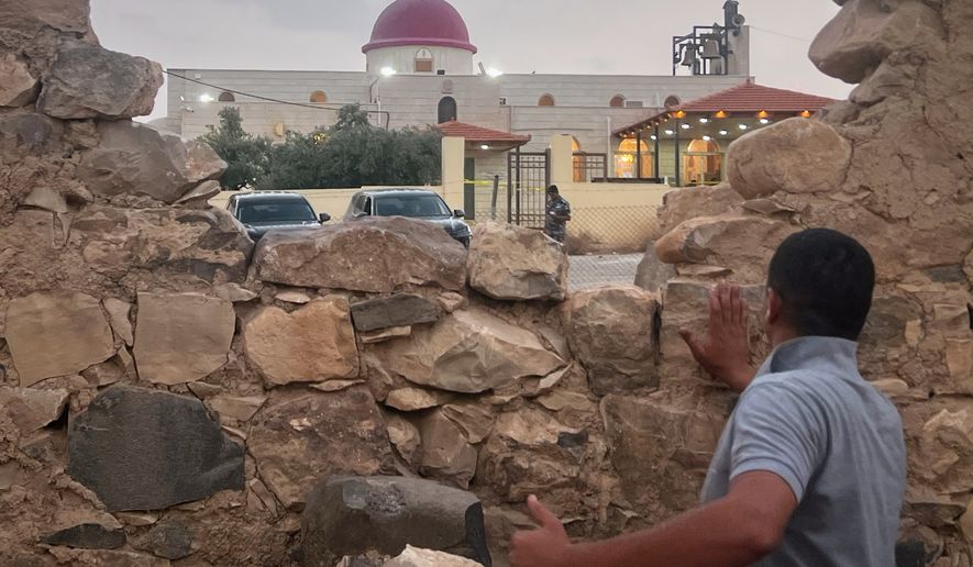 A man looks through a gap in a stone wall toward a Greek Orthodox church where gunmen opened fire during a funeral hours earlier in Hamoud village, in Jordan's Karak governorate, Friday, Oct. 23, 2026. (AP Photo)