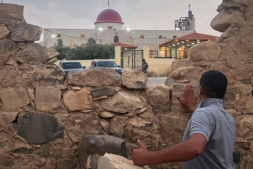 A man looks through a gap in a stone wall toward a Greek Orthodox church where gunmen opened fire during a funeral hours earlier in Hamoud village, in Jordan's Karak governorate, Friday, Oct. 23, 2026. (AP Photo)