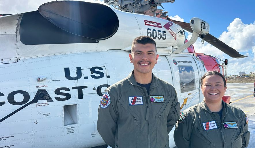 This photo made with a smartphone shows U.S. Coast Guard officer Josh Law, left, and lieutenant Miyako Miller standing in front of a rescue helicopter at the U.S. Coast Guard Air Station in Ventura, Calif., Thursday, Oct. 22, 2026. (AP Photo/Eugene Garcia)