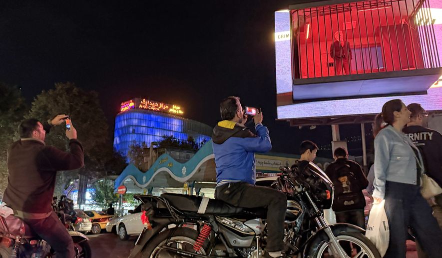 People take pictures of a billboard installation featuring an actor portraying President Donald Trump behind bars in a mock prison cell in Tajrish Square in Tehran, Wednesday, Oct. 21, 2026. (AP Photo/Vahid Salemi)