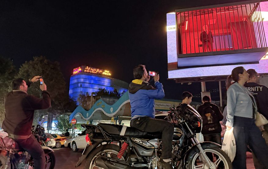 People take pictures of a billboard installation featuring an actor portraying President Donald Trump behind bars in a mock prison cell in Tajrish Square in Tehran, Wednesday, Oct. 21, 2026. (AP Photo/Vahid Salemi)