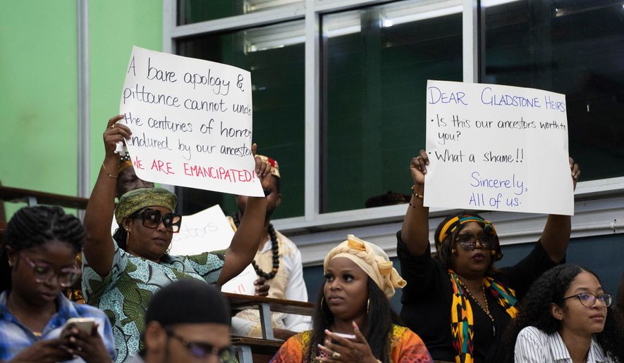 People hold signs during a speech by Charles Gladstone, a descendant of former plantation owner John Gladstone, as he delivers an apology on behalf of the Gladstone family at Georgetown University in Georgetown, Guyana, Friday, Aug. 25, 2023. (AP Photo/Chris Leung, File)