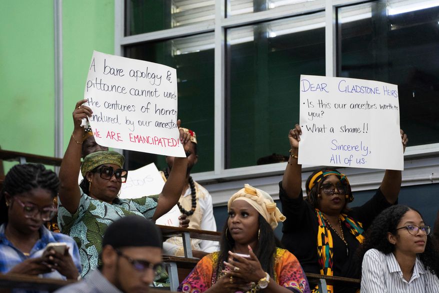 People hold signs during a speech by Charles Gladstone, a descendant of former plantation owner John Gladstone, as he delivers an apology on behalf of the Gladstone family at Georgetown University in Georgetown, Guyana, Friday, Aug. 25, 2023. (AP Photo/Chris Leung, File)