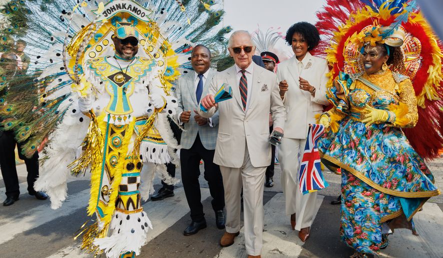 Britain's King Charles III shakes traditional cowbells as he parades with Junkanoo dancers flanked by Minister of Agriculture and Marine Resources Jomo Campbell, left, and Minister of Culture, Arts and Heritage Leslia Brice, right, during a cultural festival in Rawson Square, Nassau, Bahamas, Wednesday, Oct. 28, 2026. (AP Photo/Tim Aylen)