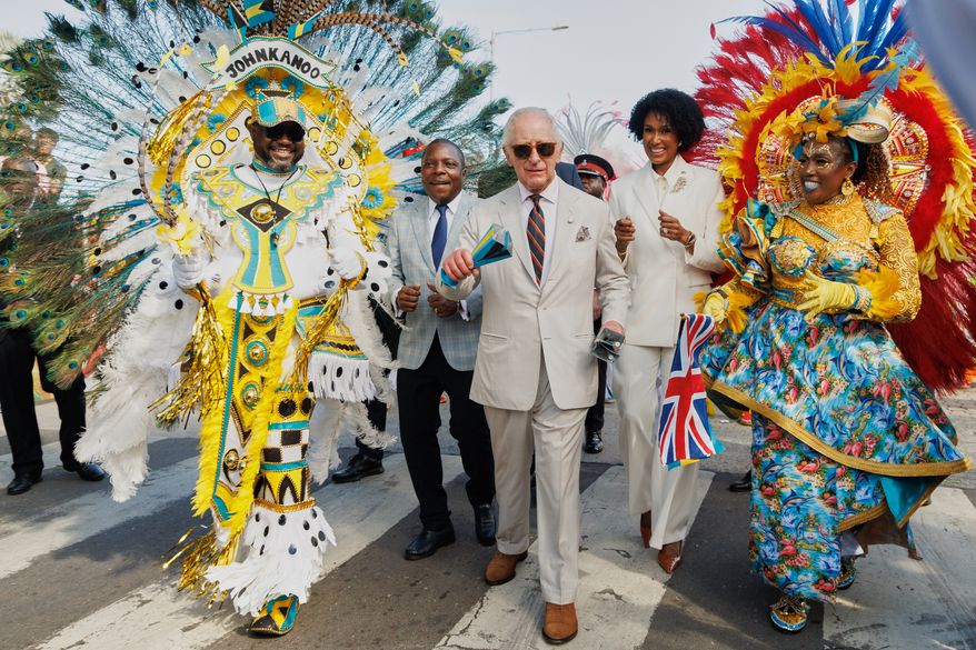 Britain's King Charles III shakes traditional cowbells as he parades with Junkanoo dancers flanked by Minister of Agriculture and Marine Resources Jomo Campbell, left, and Minister of Culture, Arts and Heritage Leslia Brice, right, during a cultural festival in Rawson Square, Nassau, Bahamas, Wednesday, Oct. 28, 2026. (AP Photo/Tim Aylen)