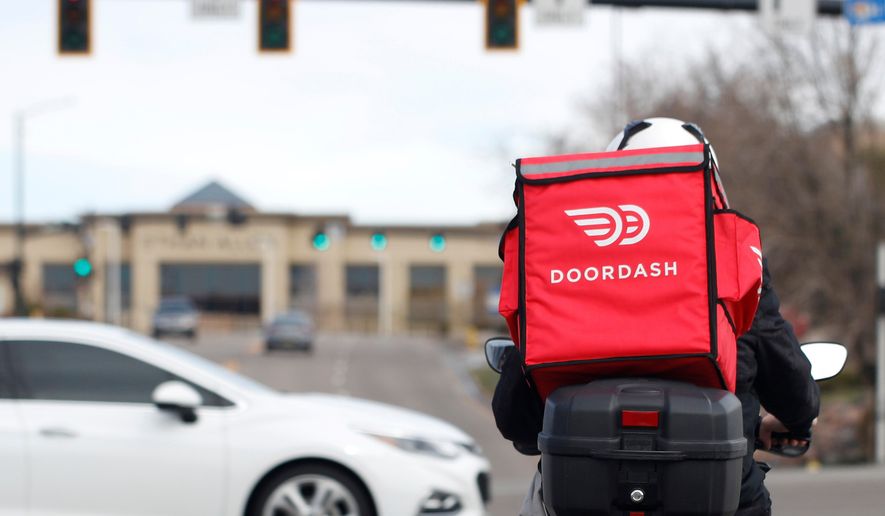 FILE - A food delivery rider waits at a traffic light, March 30, 2020, in Lone Tree, Colo. (AP Photo/David Zalubowski, File)
